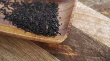 Kırsal bir ahşap yüzeyde siyah susam tohumları. Ağır çekimde düşüyorum. Kapatın. Organik sağlıklı tüm tahıl çeşnisi