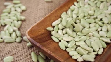 Yeşil organik verdina fasulyeleri ağır çekimde ahşap mutfak malzemelerine dökülüyor. Kurutulmuş baklagiller yakın çekim. Geleneksel İspanyol Akdeniz mutfağı konsepti. Asturias bölgesi