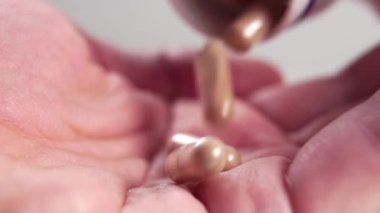 Kahverengi tıbbi kapsülleri avucunun içine yavaş çekimde dökerek. Makro atış. Reçeteli ilaç konsepti. Bulanık hap kutusu