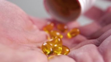 Yumuşak jel omega 3 kapsülleri avuç içine düşüyor. Beyaz bir hap kutusundaki buruşuk kuru deri ile birlikte. Ağır çekim. Makro atış. Doğal destek konsepti. Vücut bakımı fikri