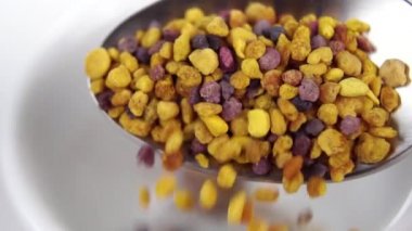 Bir çay kaşığı dolusu polen taneciği. Yavaş çekimde demlenmek için kuru taneleri beyaz çay bardağına döküyorum. Makro atış. Seçici odaklanma. Sağlıklı bitkisel içecek kavramı