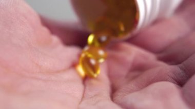 Yaşlı yetişkin adam elinde sarı omega 3 kapsülleri olan şişeden yavaş çekimde dökülüyor. Makro. İlave haplar. Sağlık hizmeti kavramı