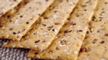 Düşen susam ve keten tohumlarıyla çıtır çıtır çıtır çıtır. Sağlıklı beslenme. Makro. Döndürme. Kaba bir kenevir kumaşın üzerinde kuru ekmek dilimleri. Tam tahıl. Yavaş çekim