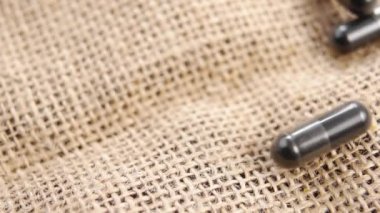 Siyah aktifleştirilmiş karbon kapsüller ağır çekimde kaba bir çuval bezi üzerine düşüyor. Makro. Etkin kömür emici haplar kapanıyor