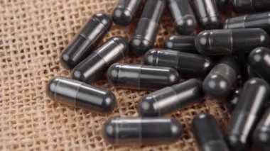 Kırsal kaba bir çuval bezi üzerinde aktif kömür kapsülleri. Makro. Yavaş dönüş. Etkin karbon hapları