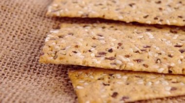 Susamlı ve keten tohumlu gevrek gevrekler. Sağlıklı beslenme yemeği. Makro. Döndürme. Kırsal bir çuval bezinde fırında ekmek dilimleri. Tam tahıl