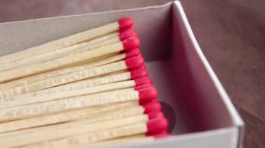 Ahşap zemin üzerinde kırmızı sülfür başları olan bir kutu dolusu kibrit. Makro. Döndürme. Ateşi yakmak için