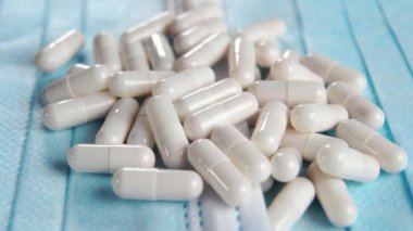 Hijyenik tıbbi mavi maske üzerine beyaz ilaç kapsülleri. Makro. Sağlık konsepti. Döndürme