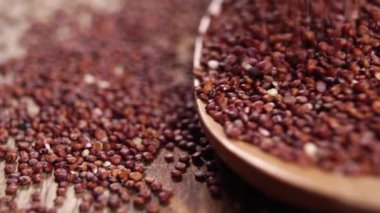 Tam tahıllı kırmızı kinoa ağır çekimde tahta bir kırsal kaşığa düşüyor. Makro. Glütensiz tohum. Çiğ süper yiyecek fikri