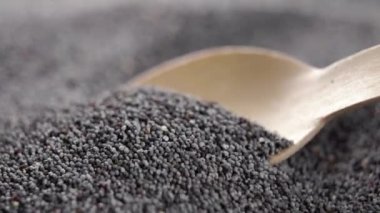Dry poppy seeds. Spooning organic black grains into a wooden spoon in slow motion. Macro shot. Vegetable super food fiber