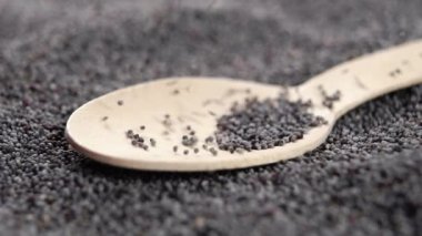 Dry poppy seeds fall into a wooden eco spoon in slow motion. Macro. Organic grain super food concept
