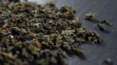 Dried leaves of chinese green tea on black kitchen slate surface. Macro. Rotation. Detailed shot