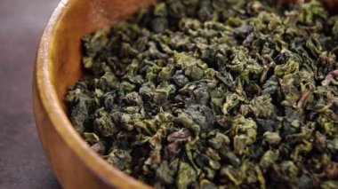 Traditional Chinese dry green tea leaves in rustic wooden bowl. Organic natural antioxidants. Macro. Rotation. Healthy ecological drink ingredient