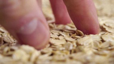 Hand takes a pinch of oat cereal flake. Falling on a heap in slow motion. Dry oatmeal porridge. Macro shot. Healthy breakfast concept