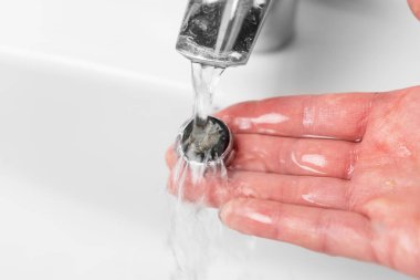Washing the clogged filter aerator of a bathroom faucet sink with calcium sediments on the plumbers hand under running water. Plumbing repair. Close-up. Sanitation concept