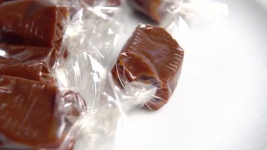 Kahverengi kremalı karamel şekerleri beyaz bir tabakta ambalajda. Makro. Döndürme
