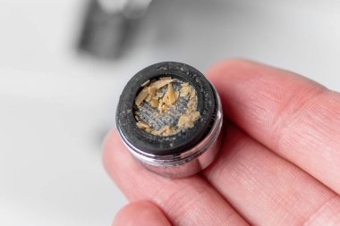 Su tesisatçısının elinde kalsiyum plaketi olan tıkanmış kirli bir musluk havalandırıcısı. Lavabonun üstündeki musluk filtresi. Makro atış. Ev bakımı konsepti. Ev ödevi fikri