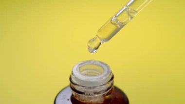 Sarı arka planda yağlı bir damlası olan kozmetik bir pipet. C vitamini parfüm sıvısı. Makro çekim