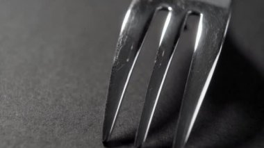 Karanlık bir masanın üzerinde siyah gölgesi olan zarif çelik çatal. Sanat restoranı servis konsepti. Makro. Döndürme