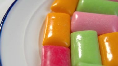 Beyaz tabakta çok renkli sakız pedleri var. Renkli çiğneme şekeri. Makro. Döndürme