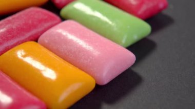 Siyah arka planda çok renkli sakız pedleri var. Renkli çiğneme şekeri. Makro. Döndürme