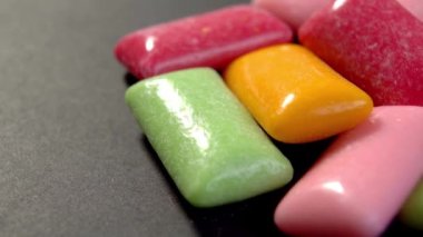 Naneli ve meyveli sakız çiğnemek. Siyah yüzeyde farklı renkte çiğneme pedleri. Makro. Döndürme