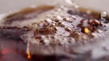Ağır çekimde köpüklü ve köpüklü buzlu bir bardağa koyu karbonatlı kola doldurmak. İçecekleri tazeliyorum. Makro çekim