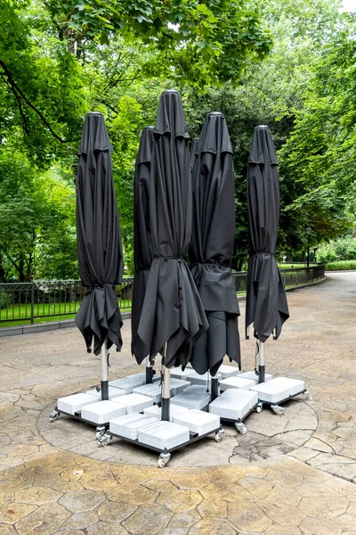 Black closed umbrellas of an empty cafe in green summer park. Outdoor exterior furniture. Vertical view