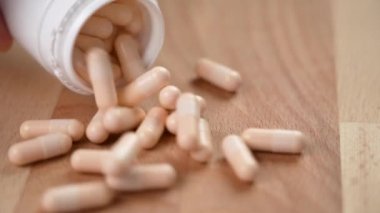 B vitamini kapsülleri, ahşap bir eko yüzeydeki beyaz plastik kaplardan yavaş çekimde düşerler.