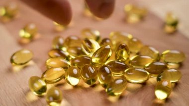 Sarı yumuşak kapsüller Omega-3. Bir el, ahşap bir eko yüzeydeki bir kazıktan balık yağı hapı alır. Doğal takviye, yakın plan.