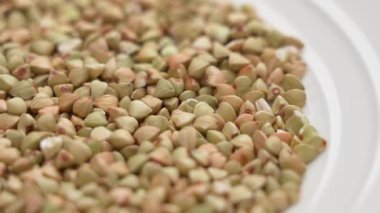 Beyaz mutfak tabağında yeşil çiğ karabuğday. Döndürme. Makro