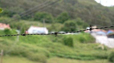 Dağlık bir kırsal çayırı çevreleyen dikenli teller ve tepede yeşil çimenler. Bulanık doğal kırsal