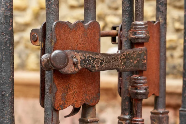 Antique iron wrought rusty latch of a locked medieval lattice gate. Vintage curved retro design