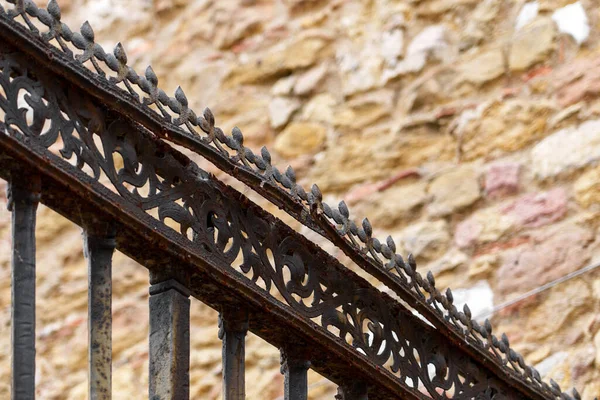 Black patterned forged iron fence with spikes and peaks of an antique medieval cathedral with a weathered stone wall in blur. Security concept