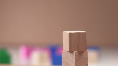Creating a block toy tower with wooden cubes. The hand sets the top of the tower in slow motion. On a background of multicolored cubic details in a blur. Close-up