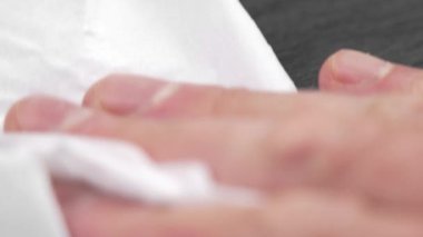 A white paper towel in hand is wiping water off a wet dark slate kitchen surface. Household hygiene and housework concept