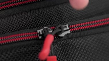 Hand unzips the zipper of a black red tourist backpack close-up
