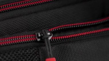 A hand closes the zipper of a black red nylon travel backpack close-up. Safety luggage on trip concept