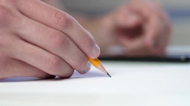 A student writing with a yellow pencil and surfing the internet on a mobile phone at a table with white paper. Business planning and educational exam concept