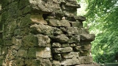 Ruin of an ancient antique stone wall of a historical building against the background of green foliage of trees. Close-up