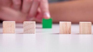 Hand moves green wooden block, stacking geometric wood cubes in a row on white table. Leadership and eco friendly lifestyle concept