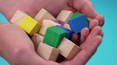 Educational wooden colorful toy blocks close-up on blue background in hands. Game building cubes