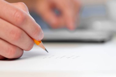Young businessman writing with a pencil and surfing the internet on a mobile phone at a table with coffee cup. Business planning concept