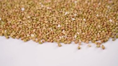 Shaking whole grain buckwheat seeds for cleaning in slow motion on white. Industrial crop cleaning at eco farm. Macro shot