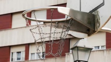 A basketball hoop with a metal chain basket on outdoor playground for street leisure game. City building on the background. Urban style view