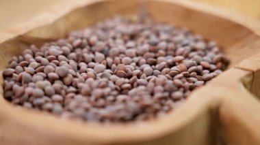 Kahverengi organik tarım mercimek tohumları kırsal bir ahşap kaseye düşüyor. Çiğ pişmemiş baklagiller