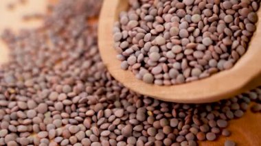 Kırsal ahşap bir kasede pişmemiş kahverengi mercimek taneleri. Yavaş çekimde mutfak tahtasına düşmek.