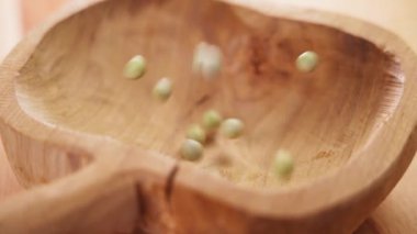 Kurumuş yeşil bezelyeler ağır çekimde kırsal bir ahşap kaseye dökülüyor. Yakın plan. Çiğ organik baklagiller. Pisum sativum, fabaceae