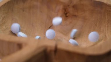 Mavi yuvarlak baş ağrısı kesiciler yavaş çekimde ahşap bir kabın içine düşüyor.