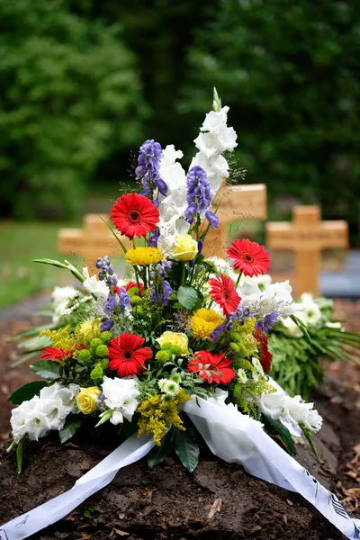 colorful flowers as grave arrangement after a funeral in front of wooden crosses in blurred background